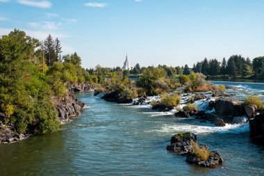 Snake river leading towards temple in Idaho falls. Beautiful view of flowing water amidst rocks and plants with sky in background. Famous tourist attraction during summer. clipart