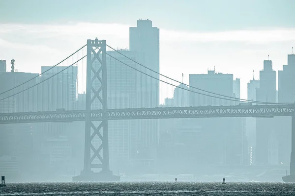 サンフランシスコの霧の多い天気の間にベイブリッジと都市のスカイラインの牧歌的な景色 背景に曇り空の海の正面に横たわっているダウンタウン地区 市内の有名な観光名所 — ストック写真