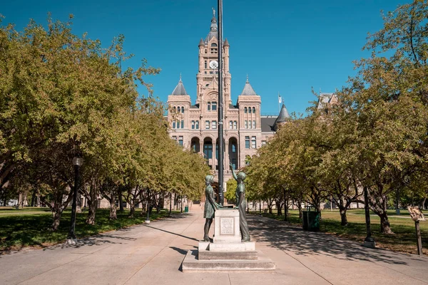 Statues at entrance of Salt Lake City and County Building. Monument sculptures amidst trees on sunny day. Famous historic Government hall with blue sky in background.