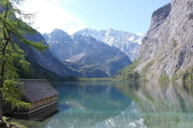 Tahta kayıkhane, sakin Alpler karlı zirveler manzarası. Sakin, masmavi bir su yüzeyi. Temiz dağ havasına ilham veriyor. Düşüncelerin berraklığının doğal zamanı. Obersee göl kıyısı, Bavyera, Almanya. Berchtesgaden Ulusal Parkı güneşli bir günde.