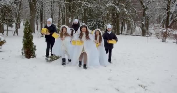 As crianças com presentes de Ano Novo correm pela floresta. Jogar na neve — Vídeo de Stock