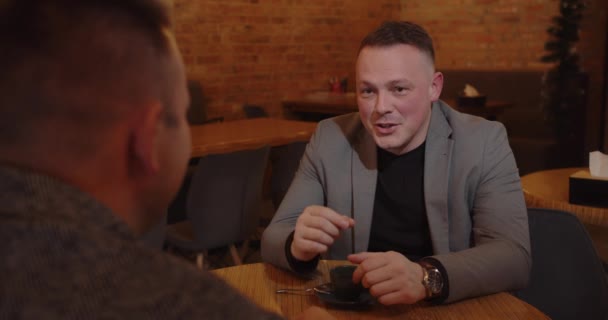 Dos hombres en un acogedor café están teniendo conversaciones de negocios y tomando café. — Vídeos de Stock