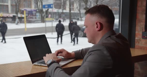 男がコンピューターで働いてる窓の外で雪が降ってる — ストック動画