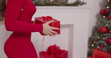 Kırmızı elbiseli kız Noel ağacının altına hediye koyar.