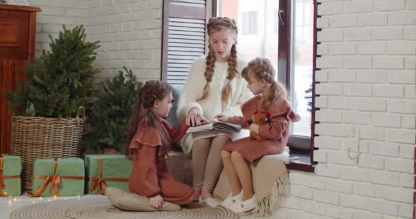 Een ouder meisje leest een sprookje voor aan haar zusjes. — Stockvideo