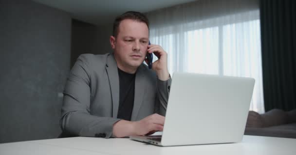 Uomo d'affari che lavora su laptop e parla su cellulare all'interno — Video Stock