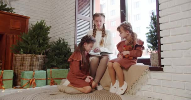 The older girl reads a fairy tale to her sisters and shows interesting pictures — Stockvideo