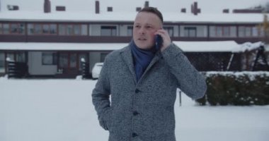 The man is focused on talking on a mobile phone and walks down a snowy street