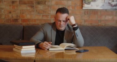 A man reads books at a table in a cafe