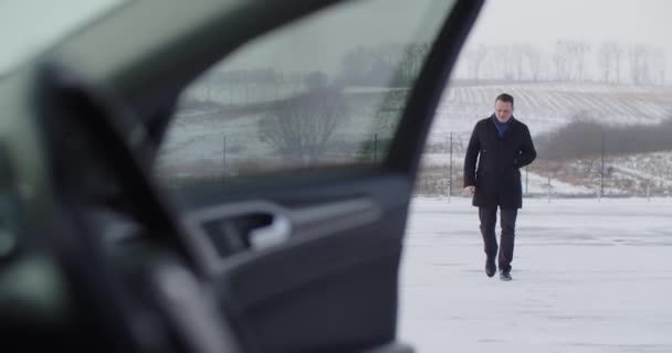 A man goes to the car on a snowy road — Stockvideo