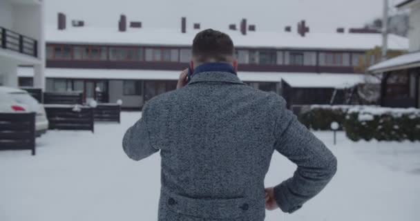 A man walks down a snowy street and talks on the phone. View from the back — Stock Video