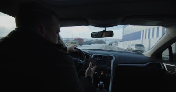In the car, the man behind the wheel is talking on the phone, moving snowy road — Wideo stockowe