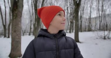 In a snowy park, a boy and his mother hold hands and talk happily