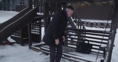 Karla kaplı salıncakta oturan bir iş adamı toplantı bekliyor.