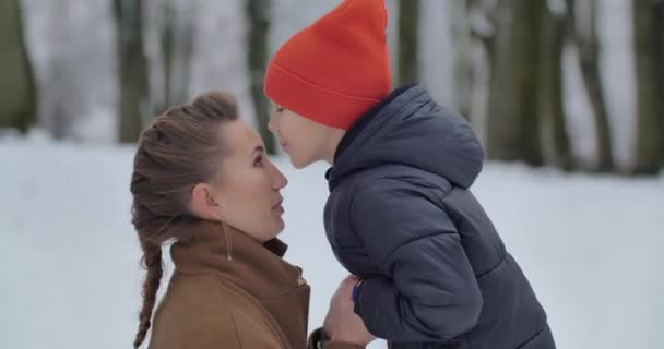 Een kleine jongen en zijn moeder lopen in een besneeuwd park. De jongen zoent moeder — Stockvideo