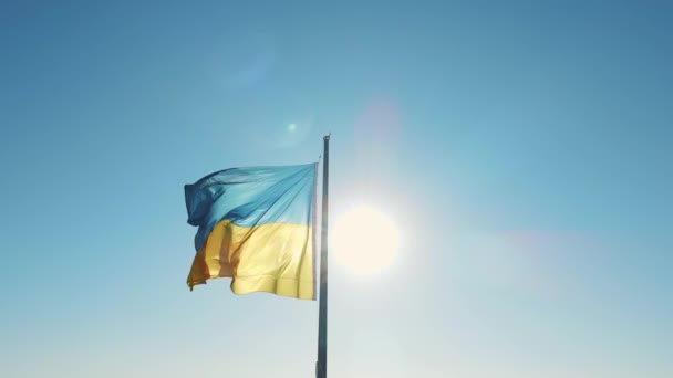 Bandera de Ucrania en el fondo del cielo azul y el sol — Vídeo de stock