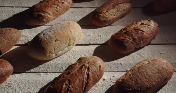 Una variedad de panes frescos se colocan sobre la mesa y se rocían con — Vídeo de stock