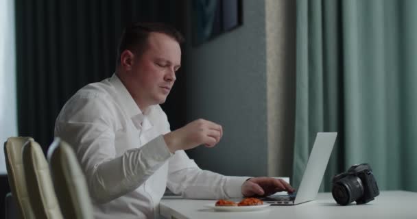 Φωτογράφος επεξεργάζεται τη φωτογραφία στο laptop και τρώει σάντουιτς — Αρχείο Βίντεο
