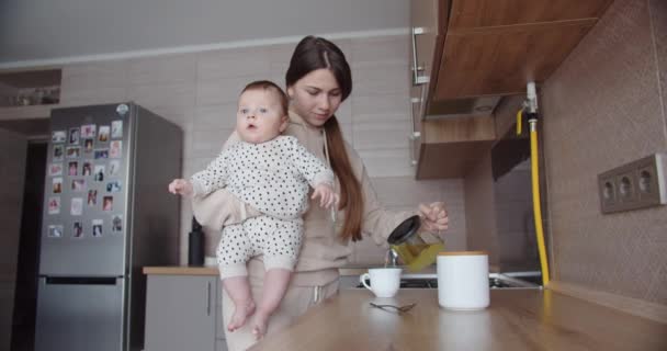 Mãe com um bebê em seus braços prepara café da manhã — Vídeo de Stock