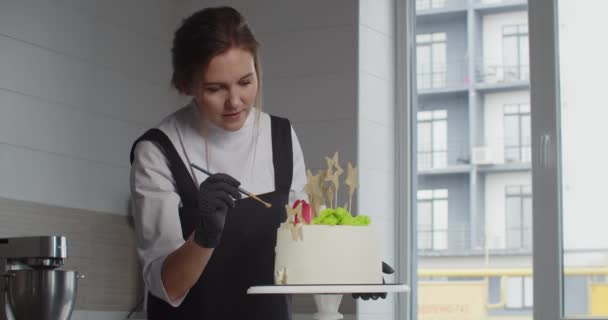 Кондитер украшает праздничный торт в кондитерской — стоковое видео