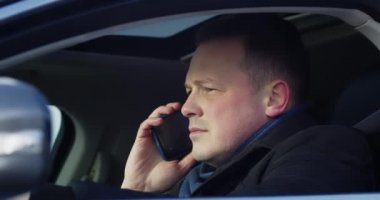 Direksiyonda oturan bir iş adamı cep telefonuyla konuşuyor.