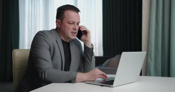 Homem de negócios focado trabalhando no laptop e falando no celular — Vídeo de Stock