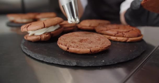 Gelukkige vrouwelijke banketbakker voegt heerlijke room toe aan chocolade chip koekjes aan tafel in de keuken — Stockvideo