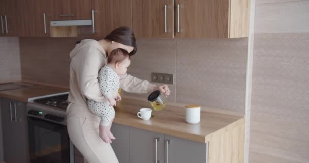 Kollarında küçük bir çocuğu olan bir anne çay yapar. — Stok video