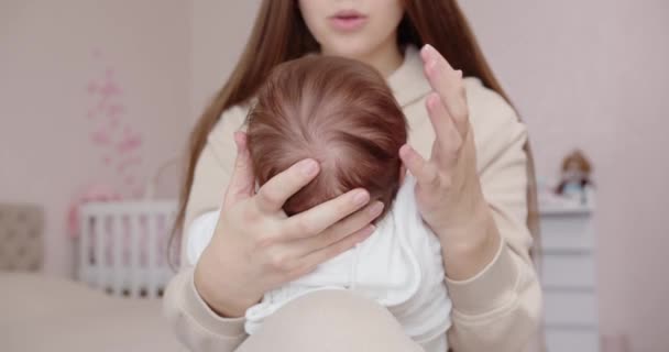 Uma jovem mãe segura seu bebê recém-nascido em seu colo e acaricia suavemente sua pequena cabeça — Vídeo de Stock