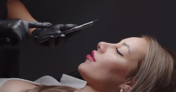 Das Mädchen mit dem Handy fotografiert das Gesicht der Kunden in einem Schönheitssalon — Stockvideo