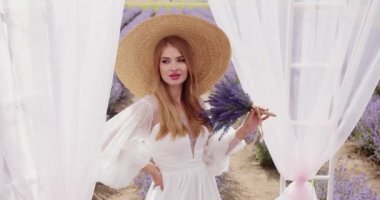 Beautiful girl in a hat with a bouquet of lavender near the gazebo. High quality 4k footage
