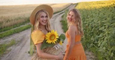 two pretty blondes are walking along a path in a field of flowers