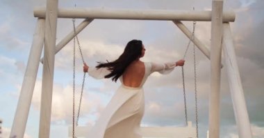 the bride in a festive dress is swinging on a swing