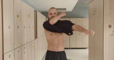 A young athlete with a nice toned body puts on a sports uniform, preparing for training