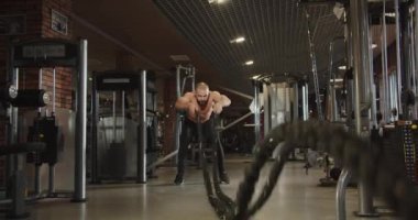 Erkek bir atlet vücudunun üst kısmını eğitmek için iki ip kullanır. İpleri ritmik bir hareketle sallıyor..