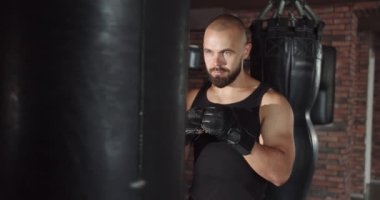 Spor üniformalı ve ellerinde bandajlarla boks yumrukları antrenmanı yapan bir adam, yakın plan. Doğru vuruş pratiği yap.