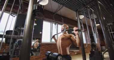 Sportsman bodybuilder with bare torso and pumping shoulder girdle, shoulder and upper limb muscles in the gym