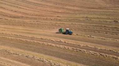 Traktör, onu yuvarlak balyalara dönüştüren özel bir tankta kurutulmuş otları topluyor. Tarım arazileri. Tarım