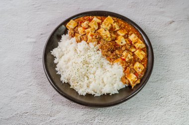 Çin yemeği mapo tofu yemeği ve siyah tabakta pirinç.