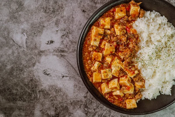 Çin yemeği mapo tofu yemeği ve siyah tabakta pirinç.