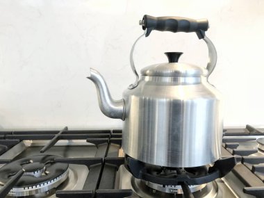 A large silver kettle with handle and spout boiling hot water on a gas stove in a home kitchen interior with copy space