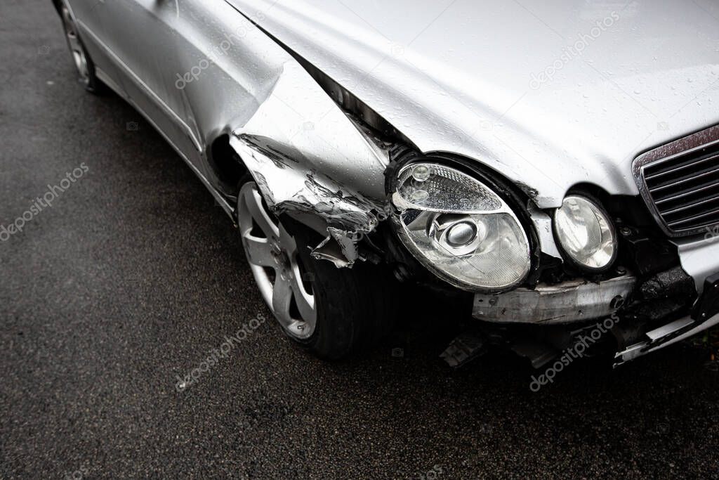 A close up of the damage to a silver car's front wing, wheel and headlights involved in a road traffic accident with copy space