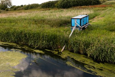 Büyük bir endüstriyel jeneratör sulama amacıyla tarla arazisine aktarmak için nehirden su pompalıyor.