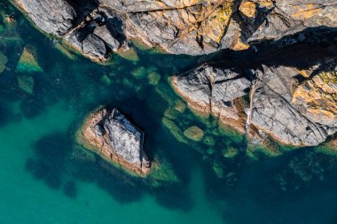 Engebeli kaya çıkıntısının tam üzerindeki hava manzarası İngiltere 'nin Cornwall şehrinde kumdan deniz yatağı olan zümrüt yeşili bir okyanusa çakılıyor.