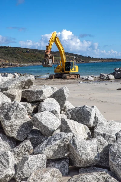 Mechanical diggers on a construction site repairing coast defences and sea walls with rocks from a quarry after rising sea levels caused erosion and damage