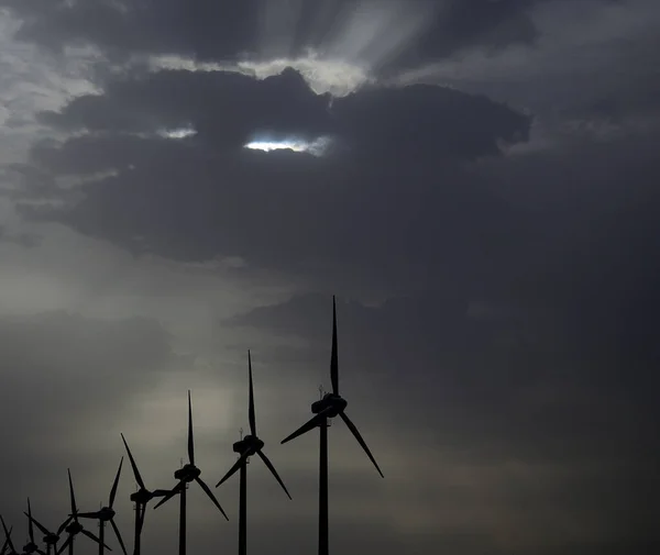 Backlit wind turbines at dawn with sun rays through the clouds