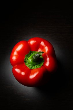 Siyah arka planda yeşil saplı kırmızı biber. Dikey fotoğraf.