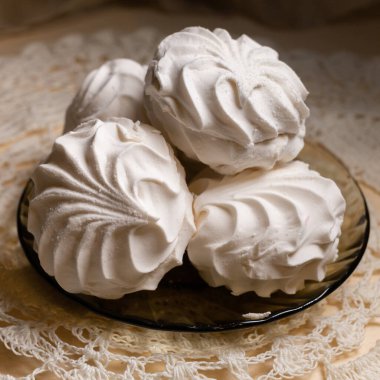 Beyaz vanilyalı şekerlemeler dantel bir peçetede küçük bir tabakta yatıyor. Kare resim.