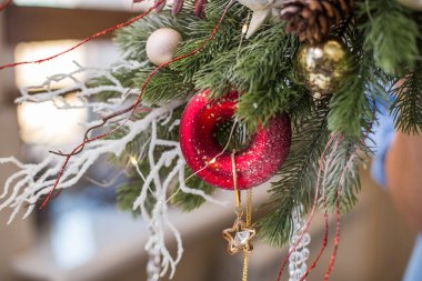 Kırmızı Noel ağacı oyuncakları ve ladin dallarından koniler içeren yeni yıl kompozisyonu bir kız tarafından tutuluyor.