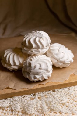 Vanilya kokulu beyaz şekerlemeler ahşap bir tahtada ve parşömen fırınında yatıyor. Dikey resim.